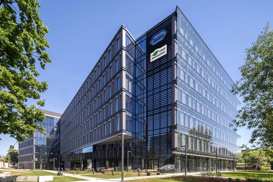 Natural Pharmaceuticals Movisan® Collagen II Nowoczesny biurowiec z przeszkloną fasadą na tle niebieskiego nieba.